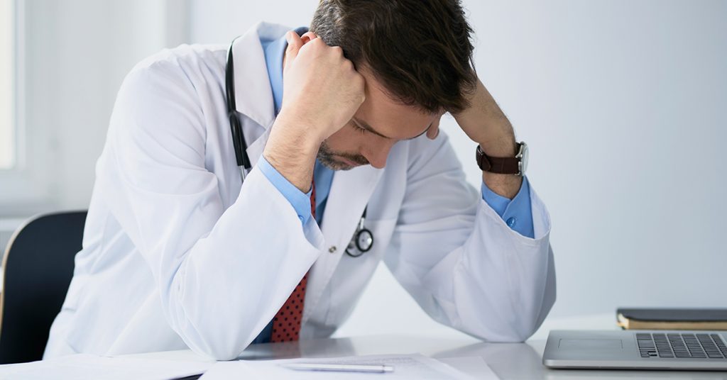 Overworked doctor doing paperwork; Blog: Tips To Prevent Physician Burnout