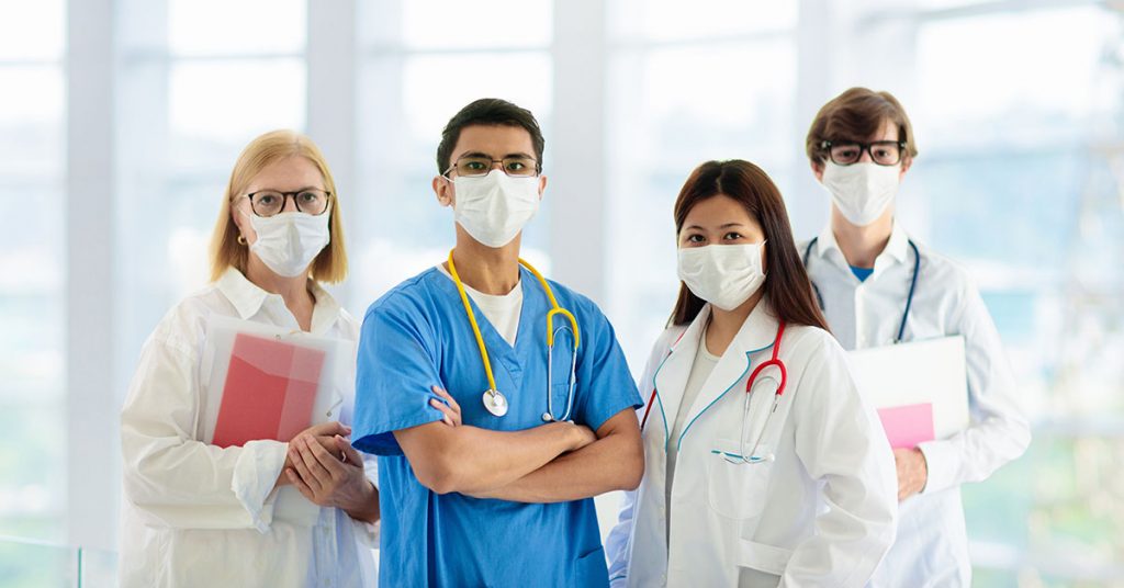 International doctor team. Hospital medical staff. Mixed race Asian and Caucasian doctor and nurse meeting. Clinic personnel wearing face mask and stethoscope. Coronavirus outbreak; blog: How COVID May Cause Permanent Changes in Healthcare