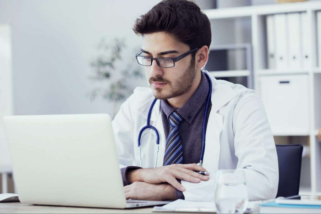 a doctor doing research on a laptop to decipher what to consider when selecting a documentation partner